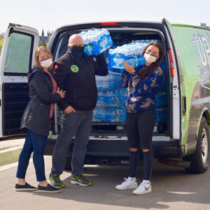 Avan full of bottles of water with Bethany Johnson (on the left, standing with each other) Husband, David Chall Daughter, Olivia Chall (on right) in front of the van.